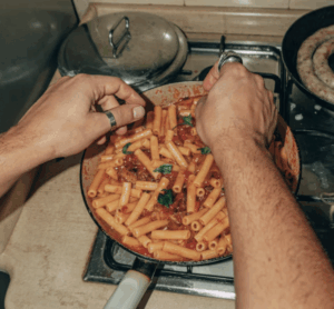 Person stirring penne pasta with tomato sauce on a stovetop.