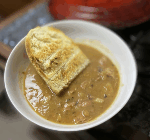 A bowl of thick brown pea soup with a slice of toasted bread on the side.