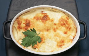 Baked dish in an oval white casserole with a golden cheese topping and parsley garnish.