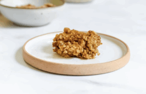 A single oatmeal cookie on a round white plate with a beige rim.