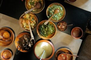 A table with wooden bowls containing vegetables, meat, and soups viewed from above.