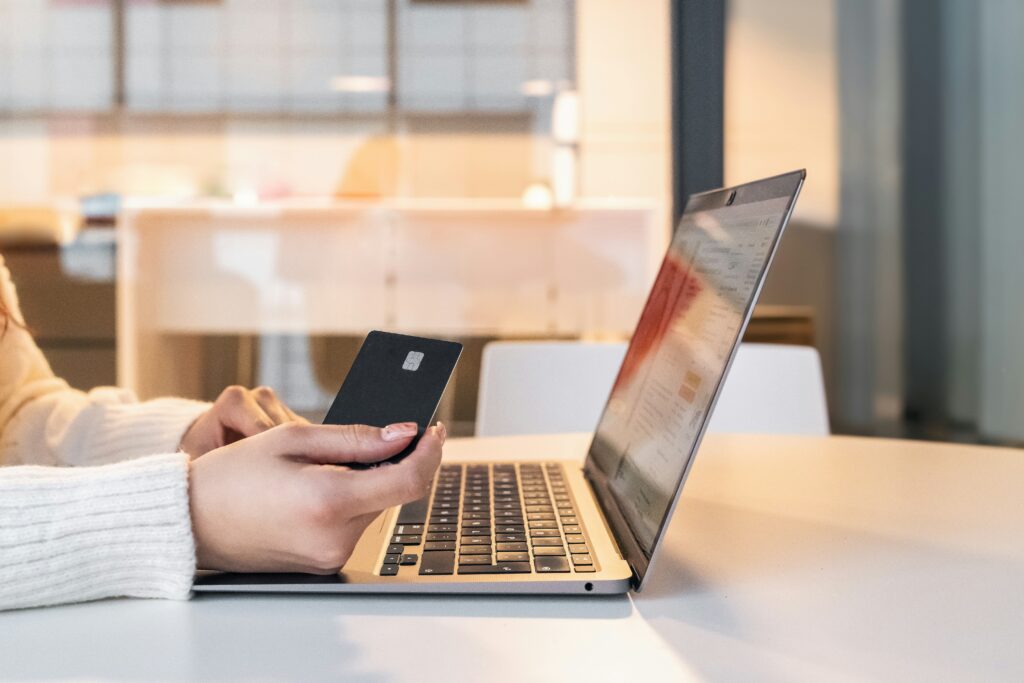 Person holding a credit card while using a laptop on a table.