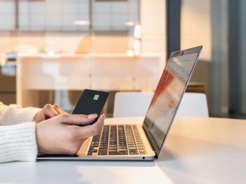 Person holding a credit card while using a laptop on a table.