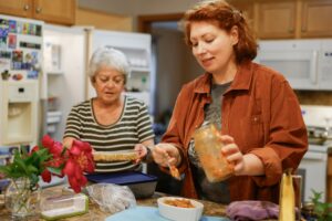 Two women preparing food in a kitchen with an open refrigerator.