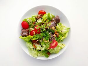 A fresh salad with lettuce, cherry tomatoes, grilled meat, nuts, and herbs on a white plate.