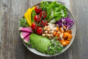 Colorful salad bowl with lettuce, cherry tomatoes, bell peppers, radish, avocado, chickpeas, sweet potato, purple cabbage, and microgreens.