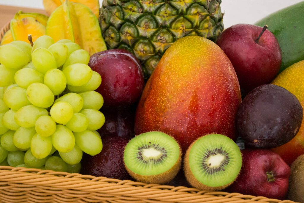 A collection of various fruits in a wicker basket, including grapes, kiwi, mango, pineapple, star fruit, apples, and plums.