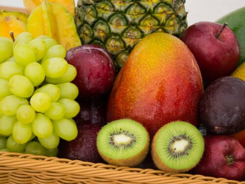 A collection of various fruits in a wicker basket, including grapes, kiwi, mango, pineapple, star fruit, apples, and plums.
