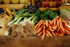 Market stall with leeks, carrots, and various produce on display.