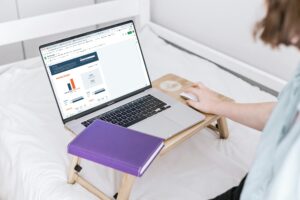 Person using a laptop displaying a budget chart on a wooden lap desk with a purple notebook.