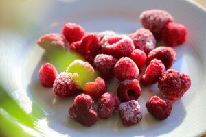 Frozen raspberries on a white plate, covered with frost and glowing in the light.