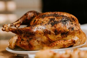 A roasted turkey with golden brown skin and blackened herbs on a white plate.