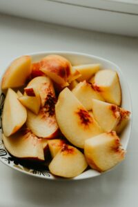 A white bowl filled with fresh peach slices, showcasing their light yellow and reddish-orange colors against a simple black floral design on the bowl.